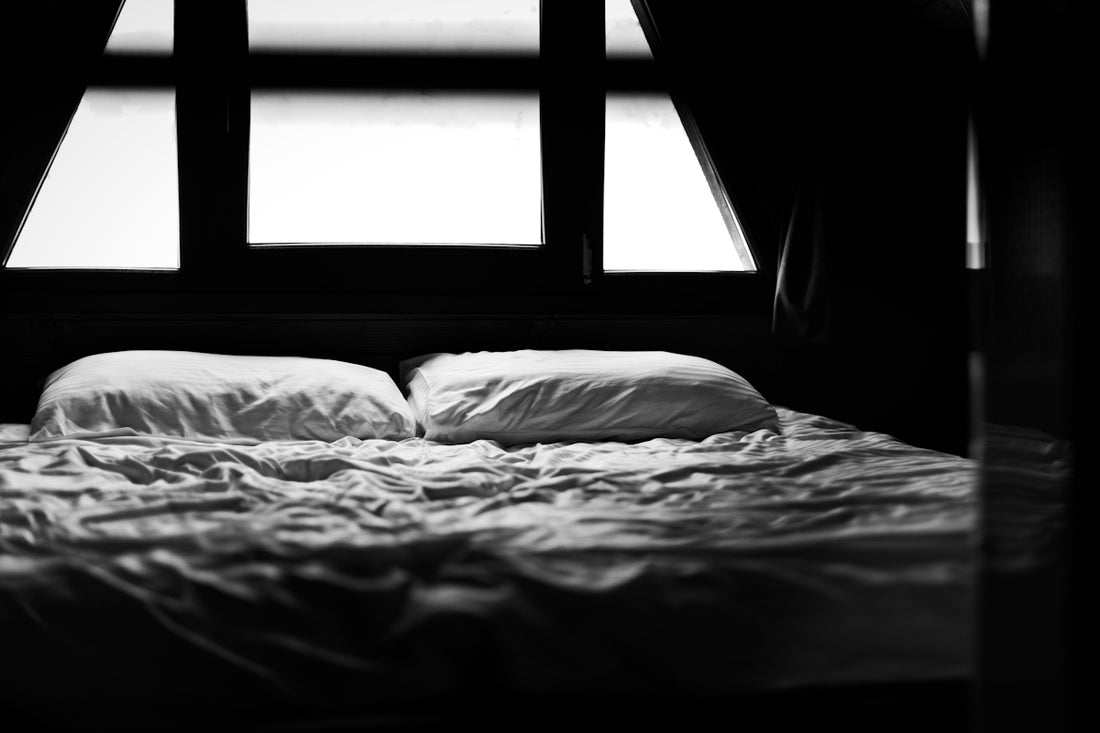 Empty bed in a dark room with bright window.