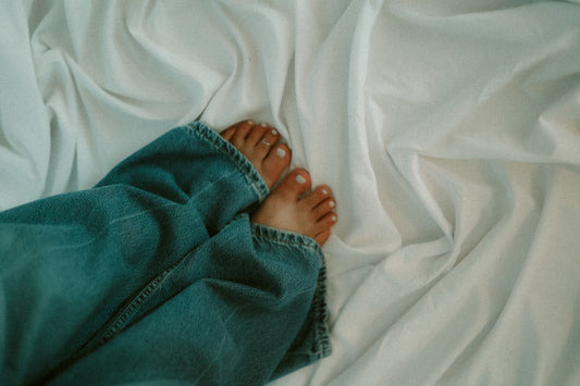 Bare feet and jeans on white sheets.