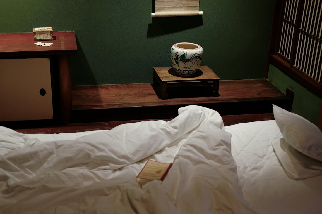 An undone bed in a dark, green room.